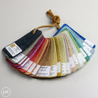 A fabric color swatch fan with multiple textured material samples in different colors, each labeled with a white tag, photographed on a light neutral background.