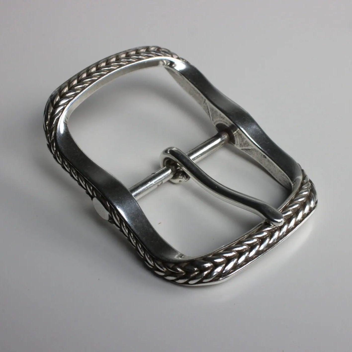 A nickel plated, bowline buckle designed for belts or straps, with intricate detailing on the edges.