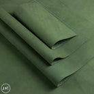 A close-up of olive green nubuck leather panels, lshown folded with a rolled corner to display its texture and color. 