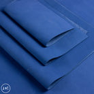 A close-up of folded blue leather, arranged diagonally on a matching blue background. 