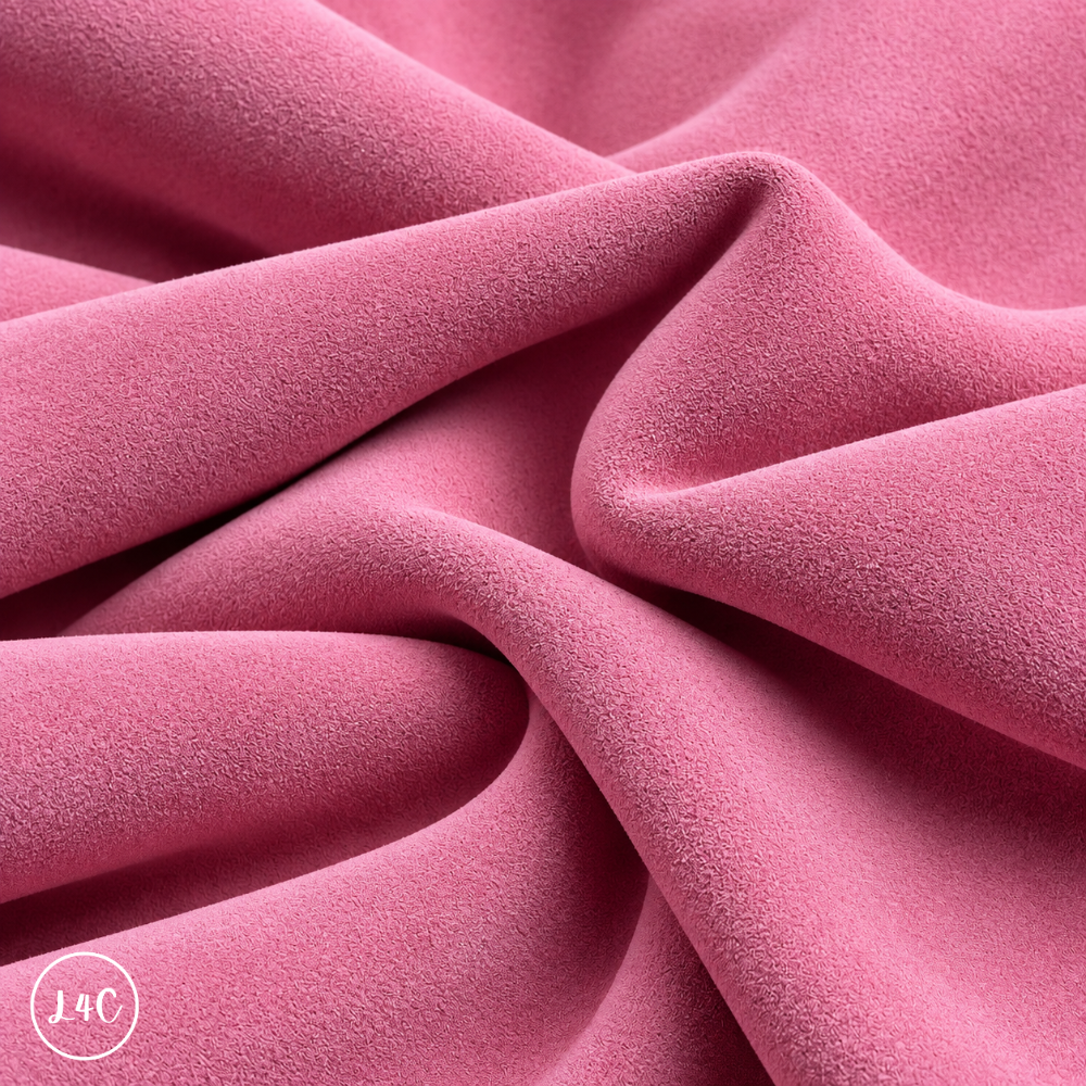 A close-up of draped light pink suede leather with a soft, plush texture, showing deep folds and shadows. 