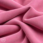A close-up of draped light pink suede leather with a soft, plush texture, showing deep folds and shadows. 