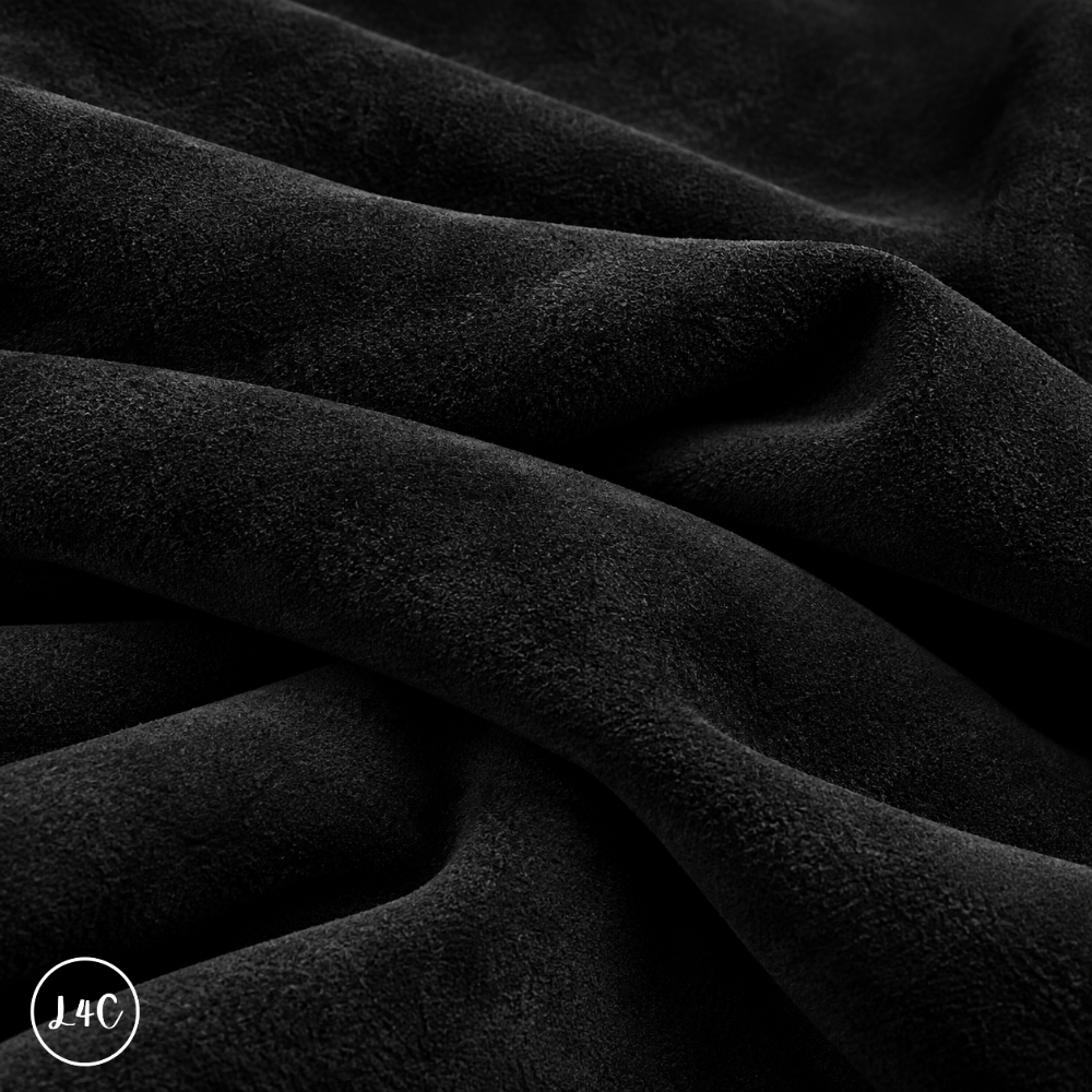 A close-up of draped black suede leather with a soft, plush texture, showing deep folds and shadows. 