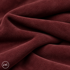 A close-up of draped burgundy suede leather with a soft, plush texture, showing deep folds and shadows. 