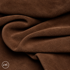 A close-up of draped chocolate brown suede leather with a soft, plush texture, showing deep folds and shadows. 
