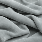 A close-up of draped light grey suede leather with a soft, plush texture, showing deep folds and shadows. 