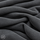 A close-up of draped grey suede leather with a soft, plush texture, showing deep folds and shadows. 