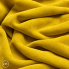 A close-up of draped yellow suede leather with a soft, plush texture, showing deep folds and shadows. 