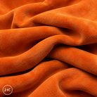 A close-up of draped orange suede leather with a soft, plush texture, showing deep folds and shadows. 