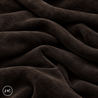 A close-up of draped dark brown suede leather with a soft, plush texture, showing deep folds and shadows. 