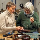 Two women working together on a craft project with tools and materials on a table.