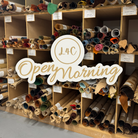 A wooden shelving unit filled with rolled fabric or carpet samples in many colors, with a large white and gold 'L4C OpenyMorning' sign overlaid across the center.