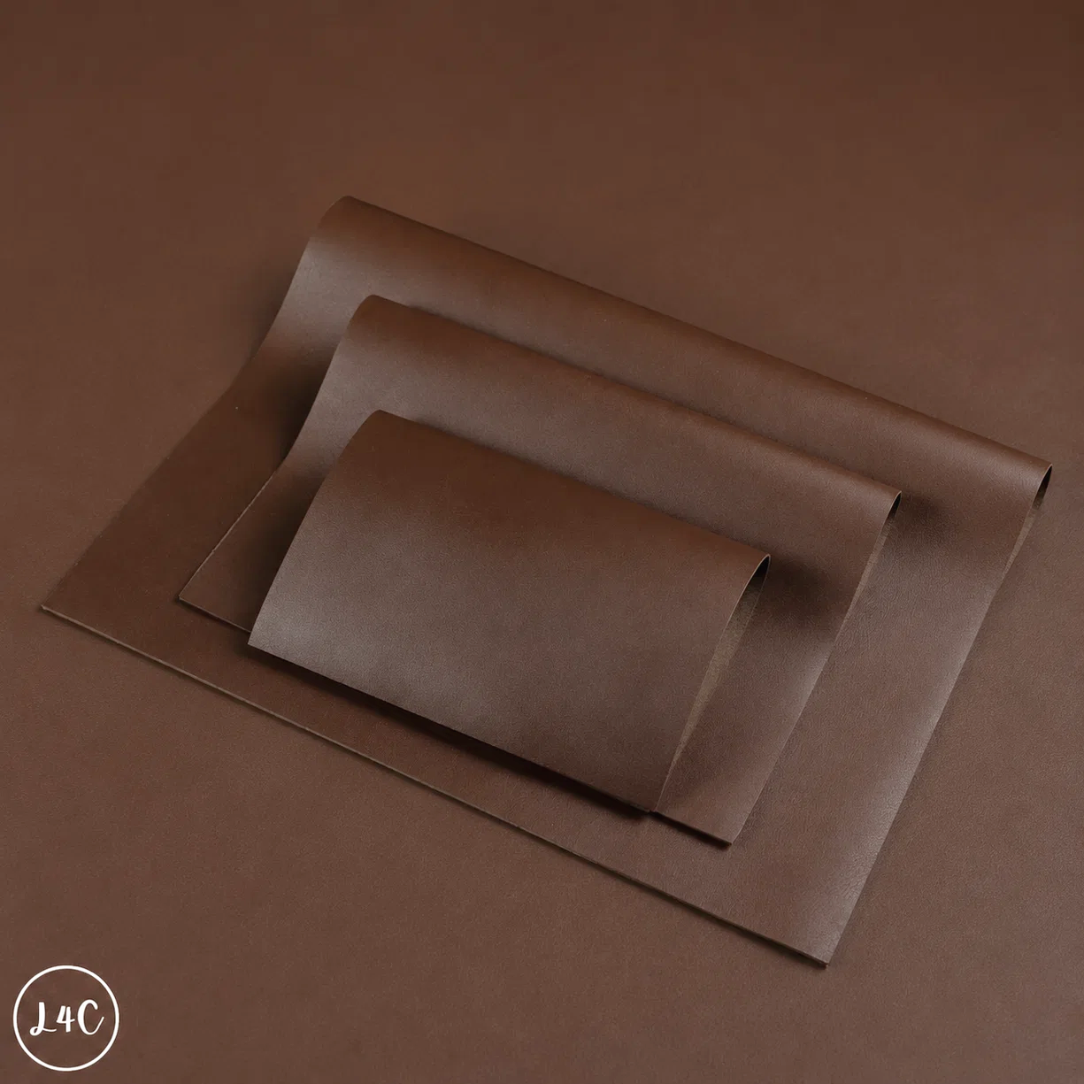 Three overlapping sheets of brown kraft paper or cardstock, with the largest sheet laid flat and the other two partially curled, on a matching brown background. 