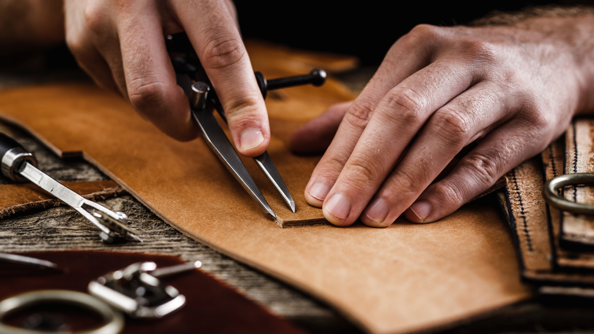 Hands using a wing divider to mark a line on a piece of leather
