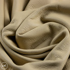 Close-up of beige textured leather with a brand logo in the corner.