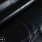 A close-up of black leather material with a smooth, slightly glossy finish and visible folds.