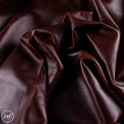 Dark brown leather fabric draped in soft folds, showing a smooth texture and rich color.