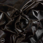 Dark brown textured leather fabric draped in soft folds, showing a glossy finish and fine grain texture.