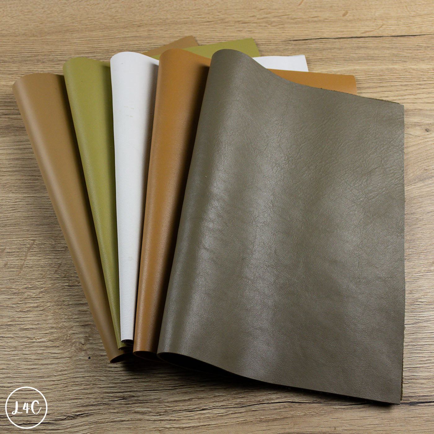 Five sheets of leather material in different colors on a wooden surface.