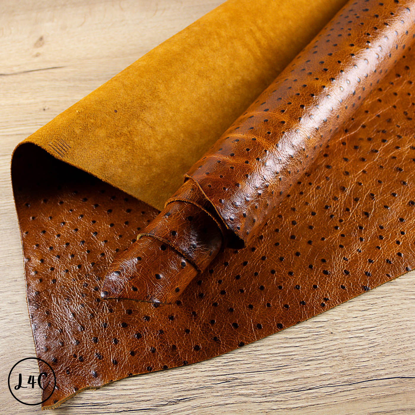 Ostrich Embossed Tan Leather Hide with perforated pattern on a wooden surface
