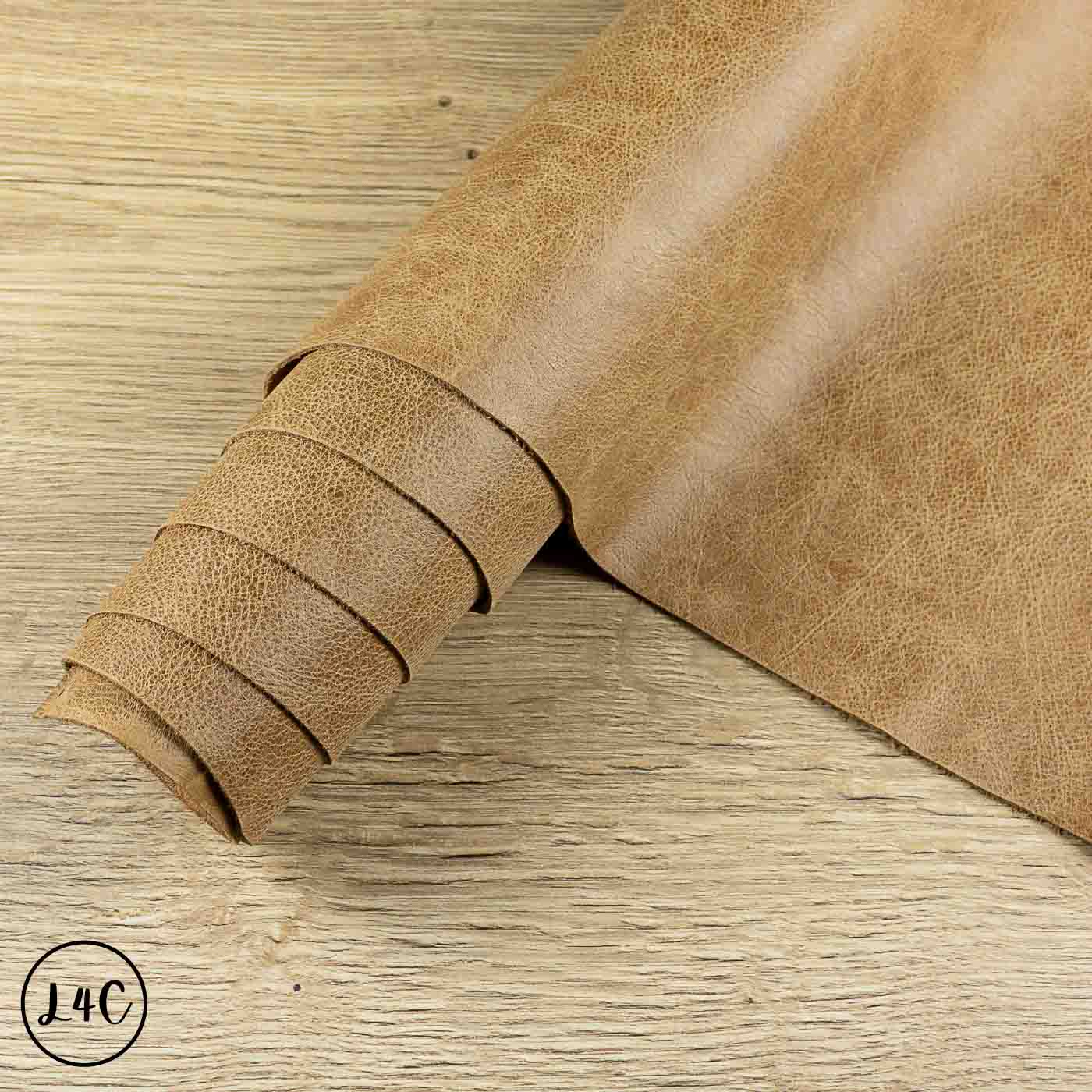 A roll of tan textured leather laid diagonally across a light wood surface.