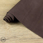 A roll of dark brown suede leather placed diagonally on a light wood grain surface.