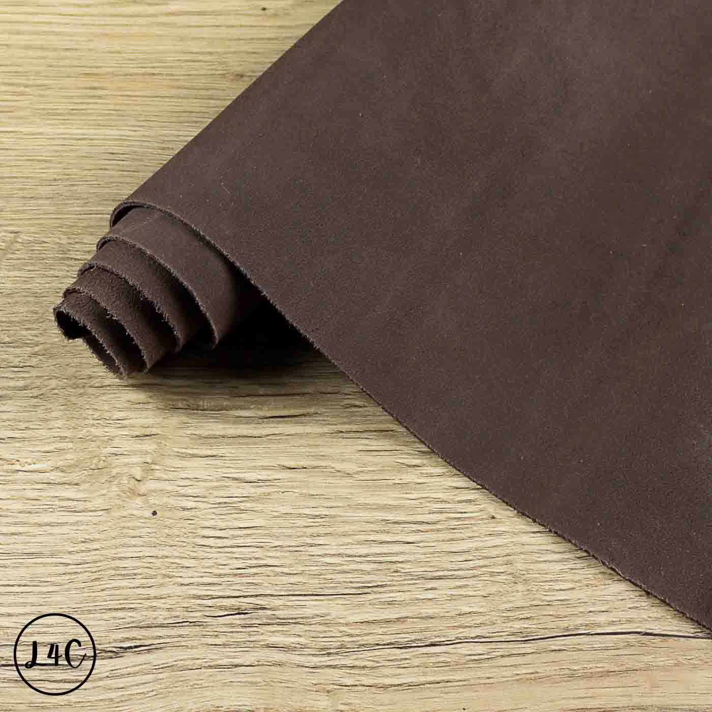 A roll of dark brown suede leather placed diagonally on a light wood grain surface.