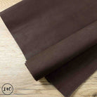 A dark brown suede leather hide roll laid diagonally on a light wood grain surface.