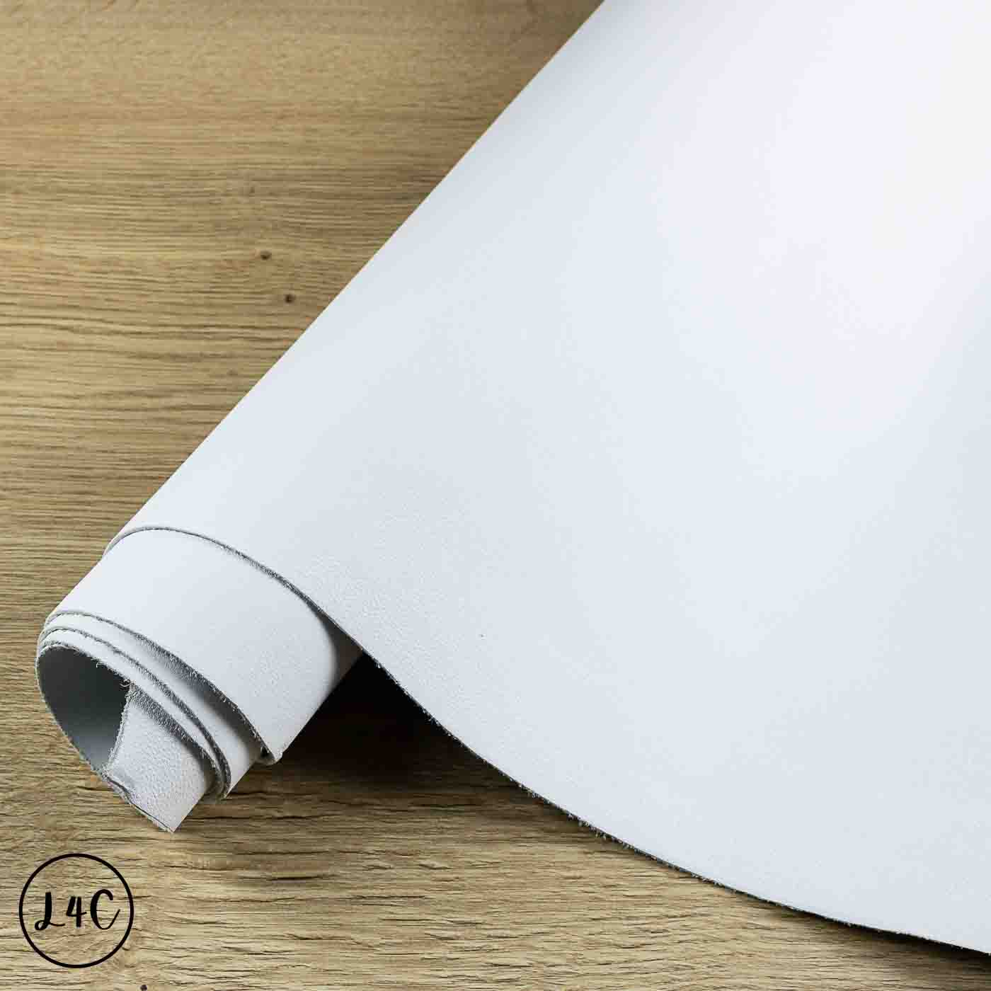 A roll of white textured leather hide, partially unrolled on a light brown wooden surface. 