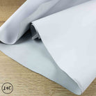 A roll of light gray leather material partially unrolled on a light wood surface.