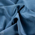 A close-up of draped dusty blue fabric with soft folds and a smooth matte texture. 